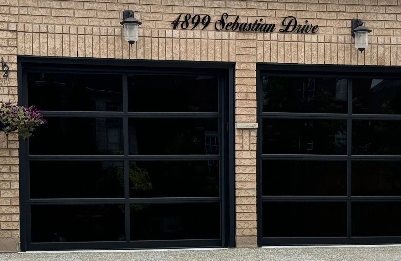Two modern full-view garage doors with black aluminium frames and tinted glass panels on a brick home.