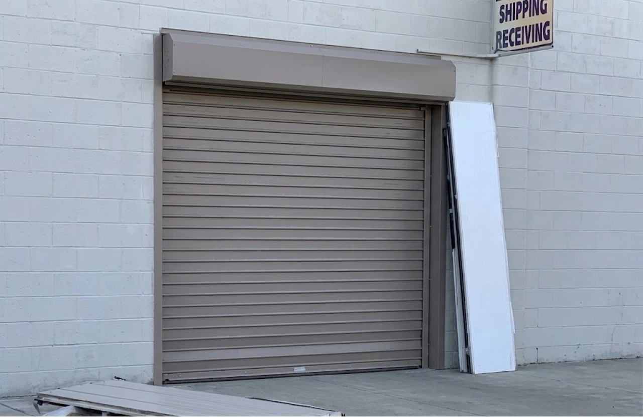 Beige commercial roll up door with interlocking slats and a coil hood at a shipping and receiving entrance.