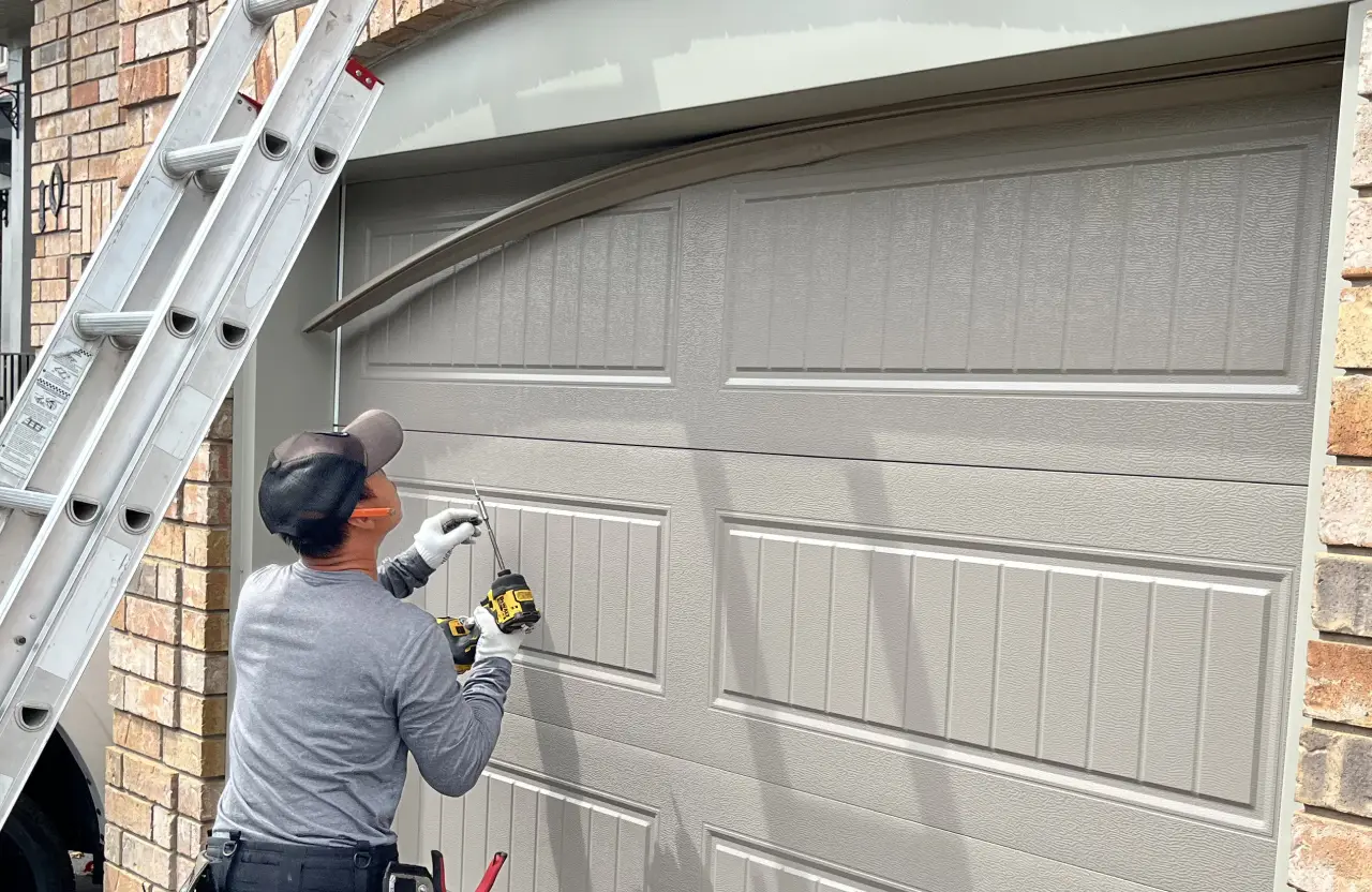 Garage door technician using a cordless drill to repair a beige sectional garage door beside an extension ladder.