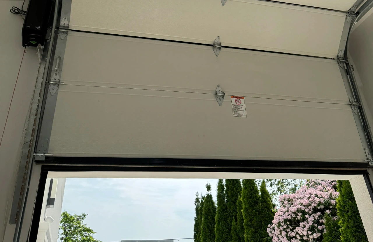 Wall mounted smart garage door opener with red emergency release cord above a partly open sectional garage door.